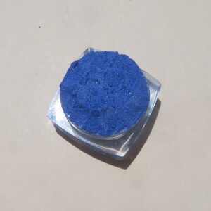 May include: A small, clear container filled with a bright blue eyeshadow powder.