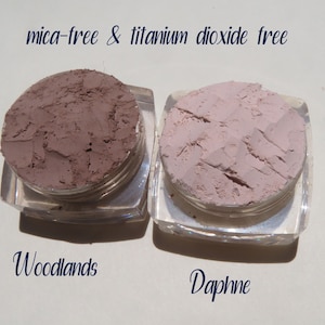 Peut inclure: Deux petits pots de poudre de maquillage min&eacute;rale en vrac, &eacute;tiquet&eacute;s "Woodlands" et "Daphne". Le texte "mica-free & titanium dioxide free" est imprim&eacute; au-dessus des pots.