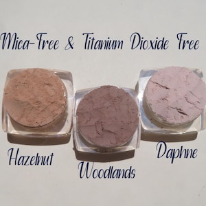 Peut inclure: Trois petits contenants de poudre de maquillage min&eacute;rale en vrac dans les couleurs noisette, bois et daphn&eacute;. Les contenants sont &eacute;tiquet&eacute;s avec les noms des couleurs. Le texte "Mica-Free & Titanium Dioxide Free" est &eacute;crit au-dessus des contenants.