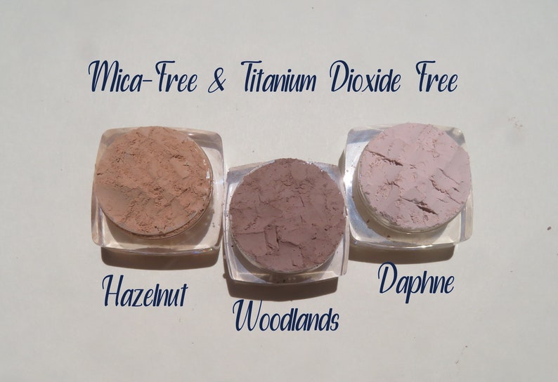 Peut inclure: Trois petits contenants de poudre de maquillage min&eacute;rale en vrac dans les couleurs noisette, bois et daphn&eacute;. Les contenants sont &eacute;tiquet&eacute;s avec les noms des couleurs. Le texte "Mica-Free & Titanium Dioxide Free" est &eacute;crit au-dessus des contenants.