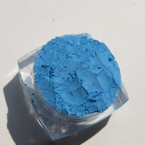 May include: A small, clear plastic container filled with a bright blue eyeshadow powder.