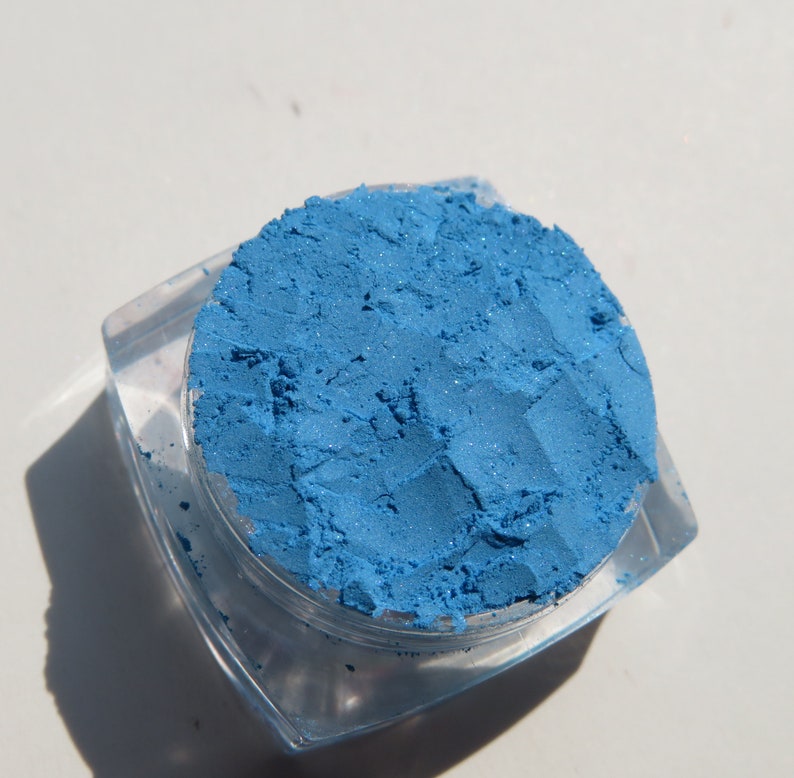 May include: A small, clear plastic container filled with a bright blue eyeshadow powder.