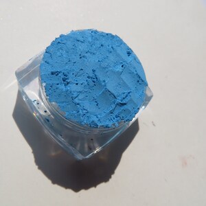 May include: A small, clear container filled with a bright blue eyeshadow powder.