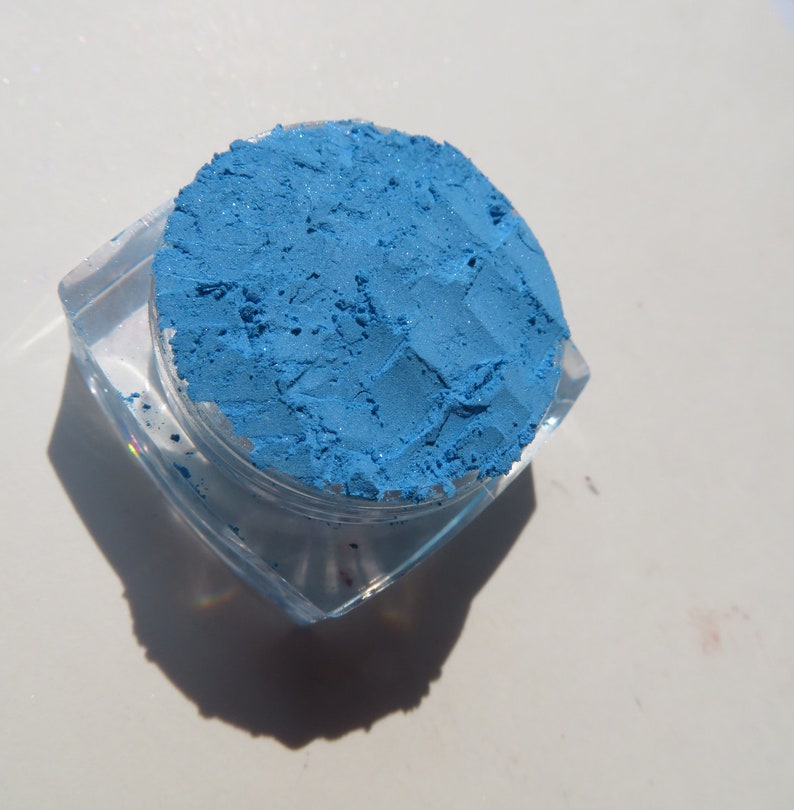 May include: A small, clear container filled with a bright blue eyeshadow powder.