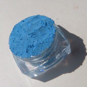 May include: A small clear container filled with a bright blue eyeshadow powder.