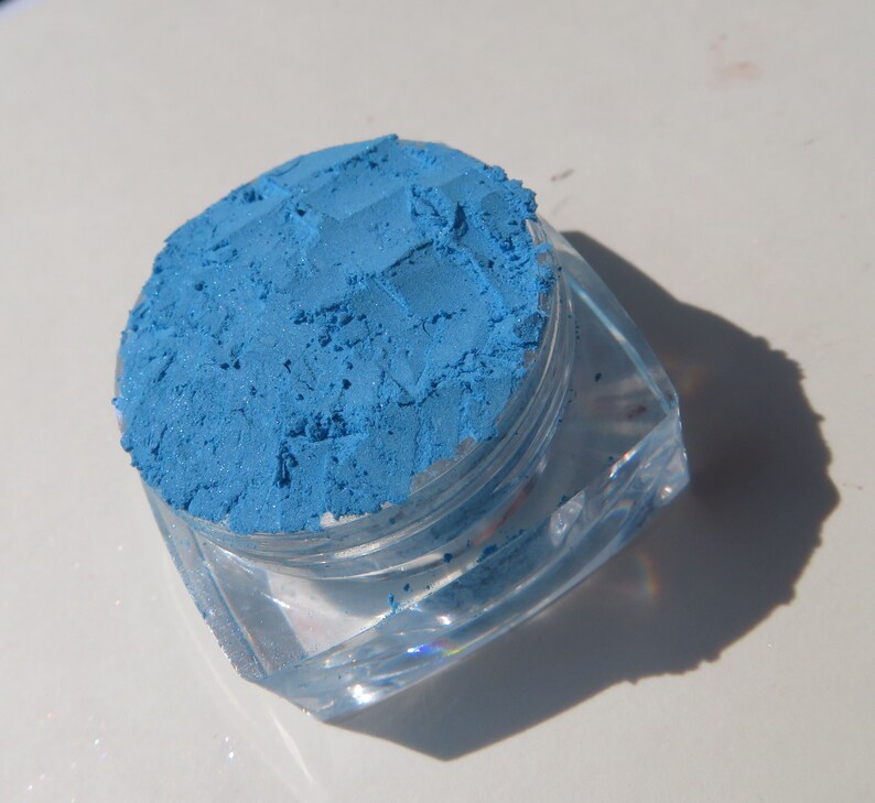 May include: A small clear container filled with a bright blue eyeshadow powder.