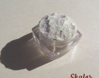 Può includere: Un piccolo barattolo trasparente pieno di glitter bianco iridescente. Il barattolo è etichettato "Skylar".