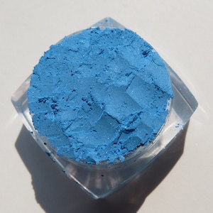 May include: A small, clear container filled with a bright blue eyeshadow powder.