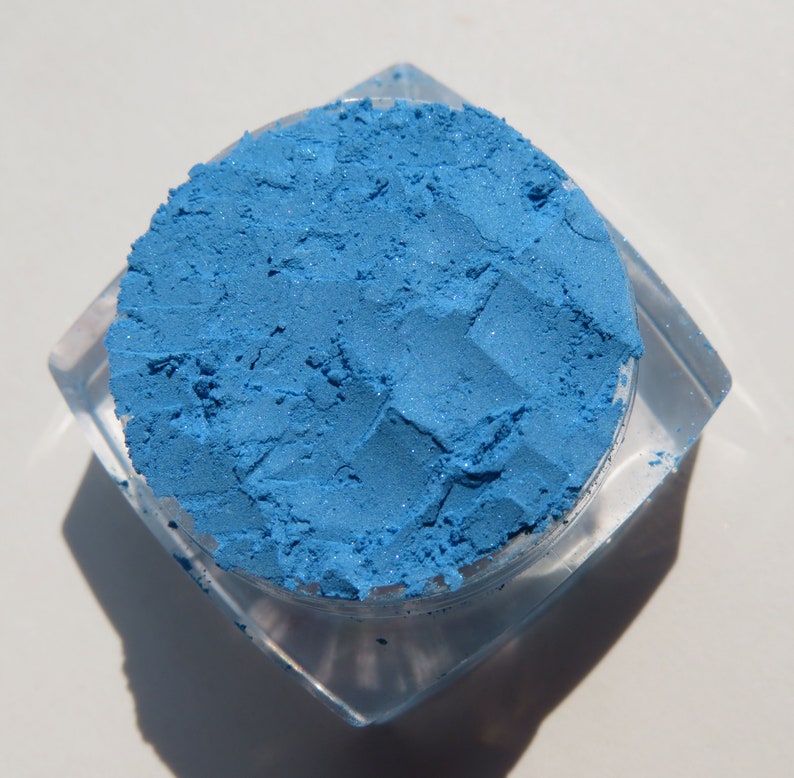 May include: A small, clear container filled with a bright blue eyeshadow powder.
