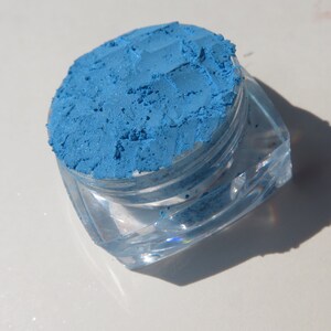 May include: A small, clear plastic jar filled with a bright blue eyeshadow pigment.