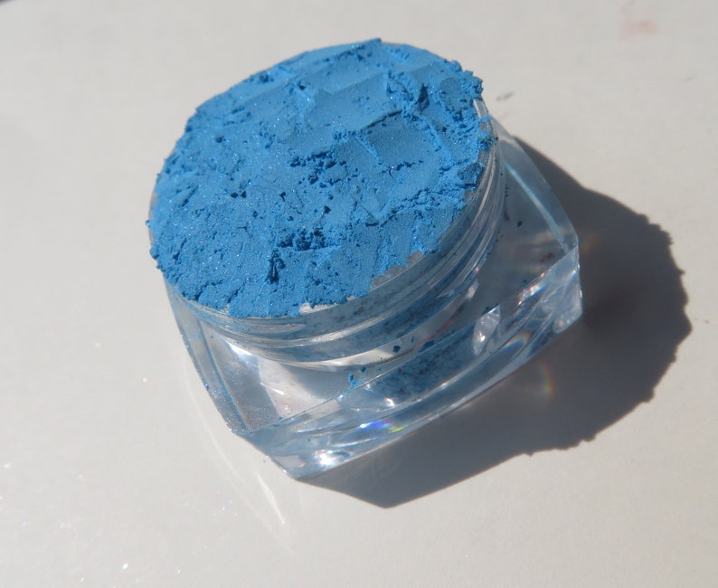 May include: A small, clear plastic jar filled with a bright blue eyeshadow pigment.