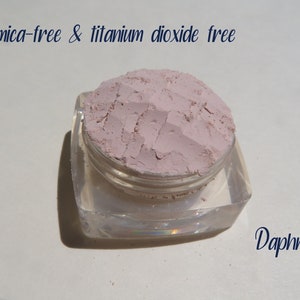 Peut inclure: Un petit r&eacute;cipient carr&eacute; transparent avec un couvercle, rempli d'une poudre rose clair. Le texte "mica-free & titanium dioxide free" est &eacute;crit au-dessus du r&eacute;cipient. Le mot "Daphne" est &eacute;crit sous le r&eacute;cipient.