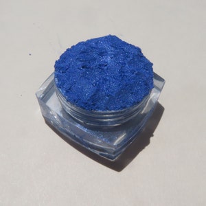 May include: A small, clear container filled with a bright blue iridescent pigment powder.