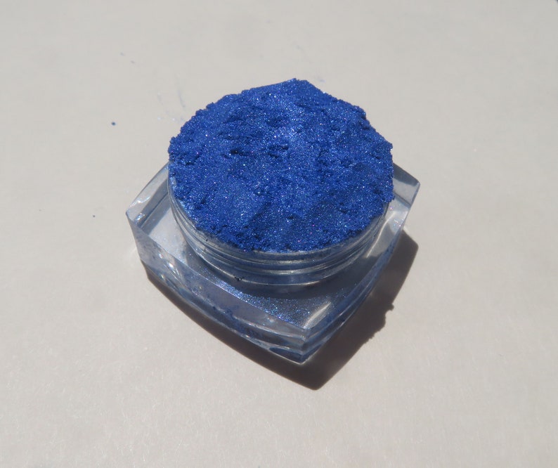 May include: A small, clear container filled with a bright blue iridescent pigment powder.