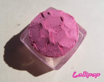 May include: A pink eyeshadow in a clear plastic container. The eyeshadow has a glittery texture and is in a compact.