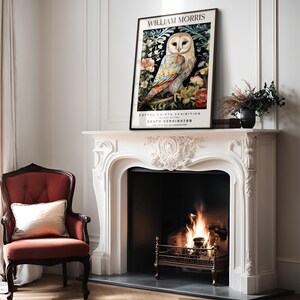 May include: A white owl with black eyes and a yellow beak is featured on a vintage poster. The poster is framed in black and has the text 'WILLIAM MORRIS COTTON PRINTS EXHIBITION SOUTH KENSINGTON' on it. The poster is hanging above a white fireplace with a fire burning inside.