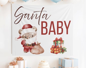 May include: A white banner with the words "Santa BABY" in brown and red. A cartoon bear dressed as Santa Claus is on the left. Presents and a cake are on a table in front of the banner. Balloons are above.