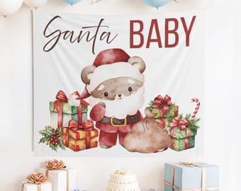 May include: A white backdrop with the words "Santa BABY" in brown script and red block letters. A cartoon bear dressed as Santa Claus is in the center, surrounded by wrapped gifts. Balloons and a cake are also present.