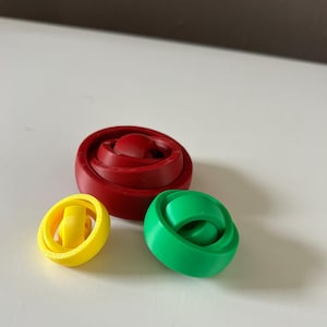 Op de afbeelding: Drie in elkaar grijpende ringen, een rode, een groene en een gele. De ringen zijn gemaakt van plastic en zijn ontworpen om op elkaar te worden gestapeld.