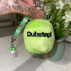 May include: A lime green plush keychain in the shape of a tennis ball with the word "Dubstep!" in black. The keychain has a beaded strand with green and white beads, and a small mushroom charm.