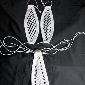 May include: White lingerie set featuring a bra and a thong, both with a net-like design. The bra consists of two oval-shaped cups, and the thong has a triangular front. White strings are attached for adjustment and tying.