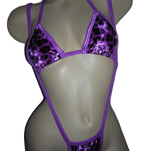 May include: A purple bikini set with a halter top and thong bottom. The fabric has a black leopard print pattern. The edges are trimmed with a matching purple fabric. The bikini is displayed on a mannequin.