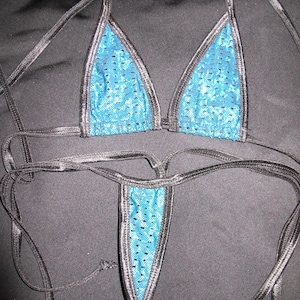 May include: A two-piece swimsuit set featuring a triangle top and a thong bottom. The swimsuit has a bright blue, perforated fabric with black trim and black ties.