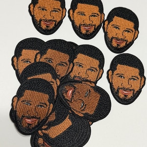 May include: A collection of embroidered patches featuring a man's face with a beard and dark hair. The patches have a black border and are arranged on a white surface. The man's face is brown with black hair and a beard.