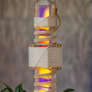 Può includere: Un portacandele in cristallo bianco con una fiamma in cima. Il portacandele è avvolto in spago bianco e marrone e ha un bagliore viola e arancione all'interno.