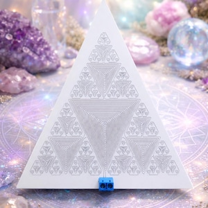 Może przedstawiać: Biały trójkątny obiekt z geometrycznym wzorem zagnieżdżonych trójkątów. Obiekt ma mały niebieski element u podstawy. Tło przedstawia kryształy, kwiaty i kule w odcieniach fioletu i bieli.