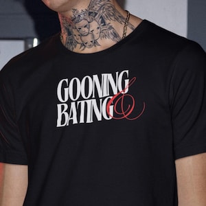 May include: A black t-shirt with the text "GOONING BATING" in white letters with a red ampersand.