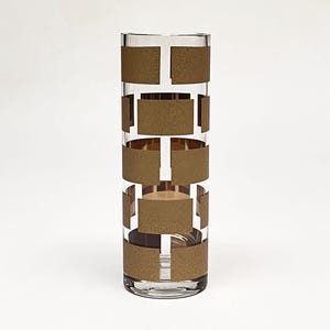 Könnte beinhalten: Eine klare Glasvase mit einem geometrischen Muster aus goldenen Quadraten. Die Vase ist hoch und zylindrisch.