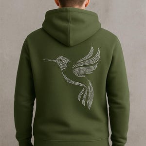 May include: Olive green hoodie with a rhinestone hummingbird design on the back. The hoodie has a hood and long sleeves. The hummingbird design is made of small, sparkling rhinestones.