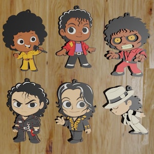 May include: Six cartoon character ornaments featuring a pop star in various outfits and poses. The ornaments include a yellow jumpsuit, a red jacket, a red suit, a black jacket, a black suit with gold accents, and a white suit with a hat.