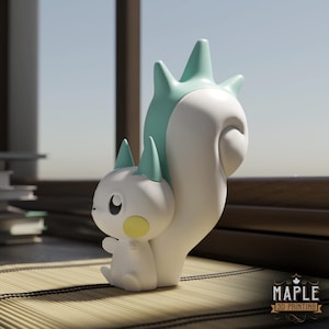 May include: A white and teal figurine of a cartoon squirrel with a large tail. The squirrel has teal ears and a teal spiky tail. The figurine has a yellow cheek and is sitting on a bamboo mat. The Maple 3D Printing logo is in the bottom right corner.