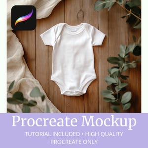 May include: White baby onesie mockup on a wooden background with greenery. The onesie is blank and ready for your design.