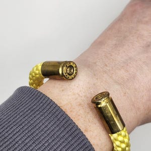 Könnte beinhalten: Ein gelbes Paracord-Armband mit einem Messing-Geschoss-Anhänger. Die Kugel trägt die Inschrift "R.P.  .38  SPECIAL"
