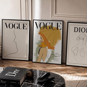 Könnte beinhalten: Drei gerahmte Wandbilder mit Modethemen. Der linke Druck zeigt eine schwarze Strichzeichnung eines Profils mit dem Text VOGUE. Der mittlere Druck zeigt eine Frau mit einem orangefarbenen Regenschirm und dem Text VOGUE. Der rechte Druck zeigt eine schwarze Strichzeichnung eines Rückens mit dem Text DIOR.