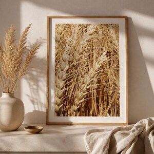 Könnte beinhalten: Ein gerahmter Wandkunstdruck mit einer Nahaufnahme von goldenen Weizenähren auf einem Feld. Der rechteckige Druck befindet sich in einem hellen Holzrahmen und zeigt detaillierte Texturen der Ähren und Halme in warmen, erdigen Beige- und Brauntönen.