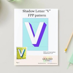 May include: A white paper with the text "Shadow Letter V FPP pattern" and a large letter "V" in white and purple. A smaller image of the letter "V" is in the lower left corner. A pencil and a green notebook are on the right.
