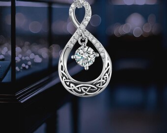 Puede incluir: Collar con colgante plateado con diseño de símbolo infinito. El colgante tiene forma de lágrima con un diseño de nudo celta en la parte inferior, adornado con cristales transparentes y una piedra preciosa redonda central brillante.