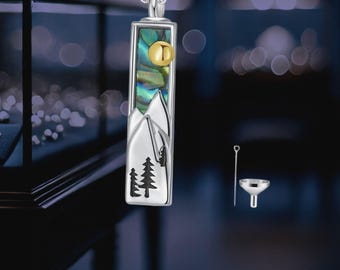 May include: Silver necklace with a rectangular pendant featuring a mountain scene with a small gold sun. The pendant is made of abalone shell with a blue and green iridescent finish. The necklace comes with a small funnel and a silver chain for filling the pendant.