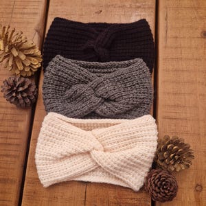 Könnte beinhalten: Drei gestrickte Stirnbänder in verschiedenen Farben: Schwarz, Grau und Creme. Die Stirnbänder sind verdreht und haben einen Knoten in der Mitte.