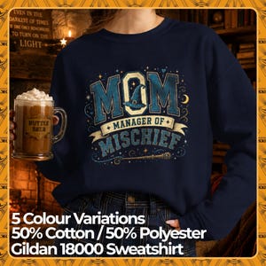 Puede incluir: Una sudadera azul marino de cuello redondo con un estampado gráfico que dice MOM MANAGER OF MISCHIEF en letras azules y doradas. El diseño incluye un sombrero de bruja, una varita mágica, estrellas y una luna creciente de algodón y poliéster.