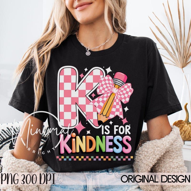 May include: Black t-shirt with a colorful graphic that says "K is for Kindness." The design features a pink and white checkered "K" with a pencil and bow. The text "Kindness" is in rainbow colors.
