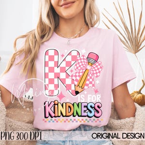 May include: Pink t-shirt with a graphic design featuring a large letter "K" in a pink and white checkered pattern, a pencil with a pink bow, and the words "K IS FOR KINDNESS" in colorful letters. The shirt also has the text "PNG 300 DPI ORIGINAL DESIGN".