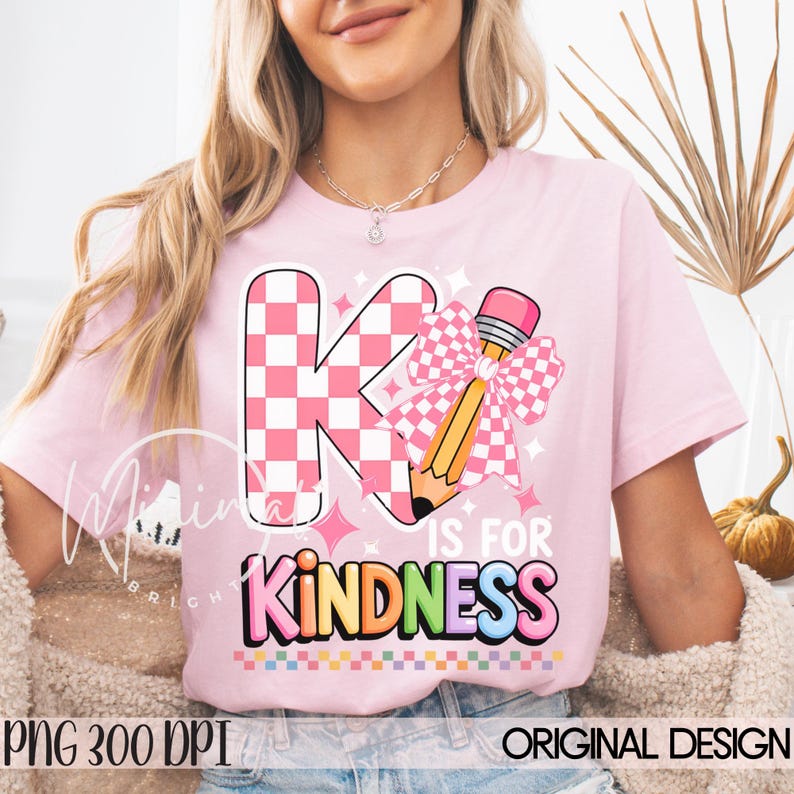 May include: Pink t-shirt with a graphic design featuring a large letter "K" in a pink and white checkered pattern, a pencil with a pink bow, and the words "K IS FOR KINDNESS" in colorful letters. The shirt also has the text "PNG 300 DPI ORIGINAL DESIGN".