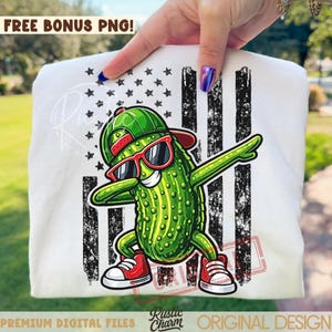 Könnte beinhalten: Weißes T-Shirt mit einem Cartoon-Gurken-Dabbing, das eine grüne Kappe, rote Sonnenbrille und rote Turnschuhe trägt. Das Design enthält eine amerikanische Flagge mit schwarzen Streifen und Sternen. Der Text "FREE BONUS PNG!" steht oben.