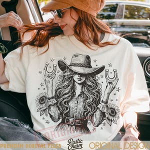 Puede incluir: Camiseta color crema con una ilustraci&oacute;n detallada de una mujer con sombrero de vaquero sosteniendo herraduras, rodeada de estrellas y girasoles. El dise&ntilde;o tiene una est&eacute;tica vintage y r&uacute;stica. El texto "Rustic Charm" y "Original Design" tambi&eacute;n es visible.