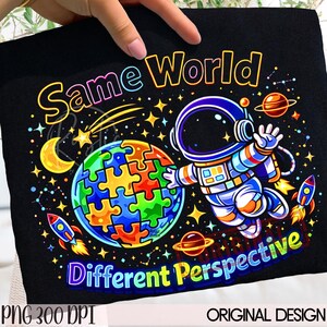 May include: Black graphic tee with the words "Same World, Different Perspective." The design features an astronaut, a colourful puzzle-piece globe, rockets, planets, stars, and a crescent moon.